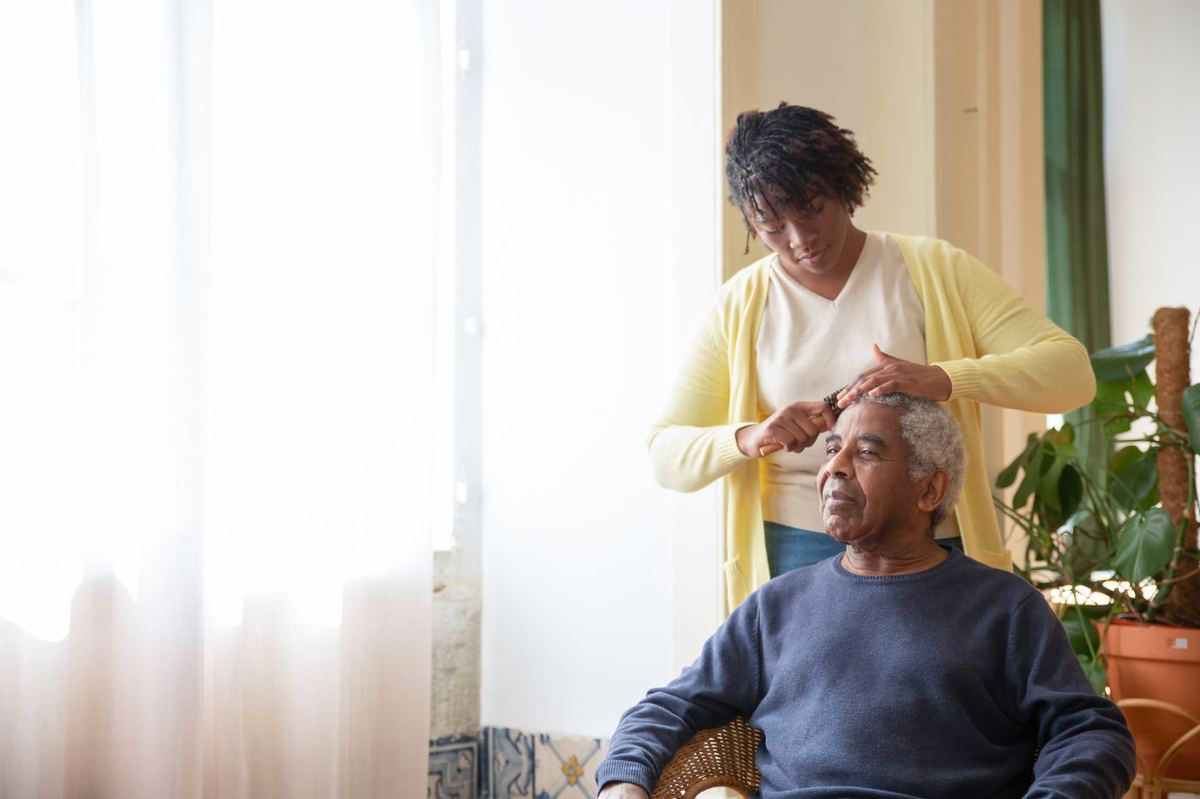 Caregiver gently combing a senior man's hair by a sunlit window