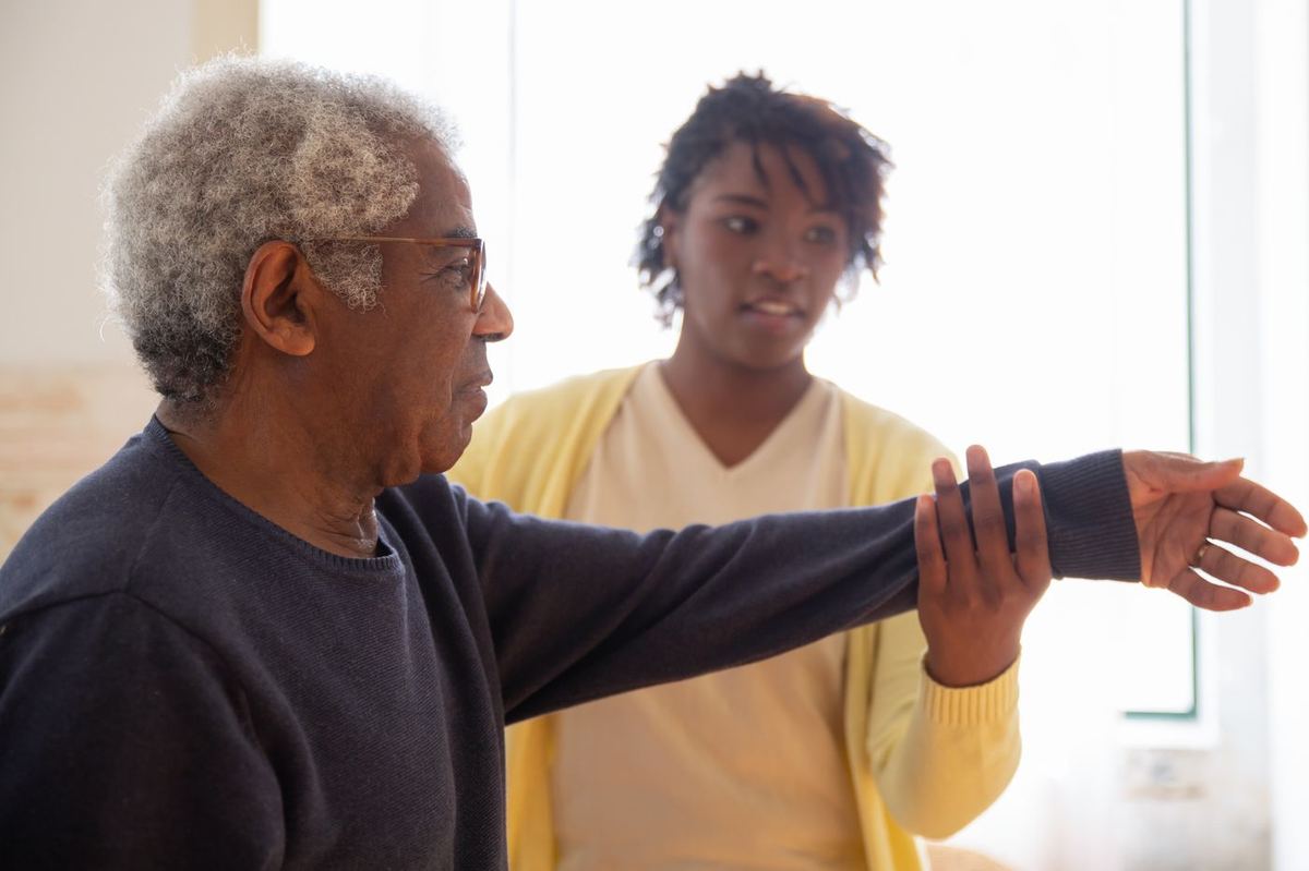 Caregiver guiding a senior man through gentle arm exercises in a bright living room