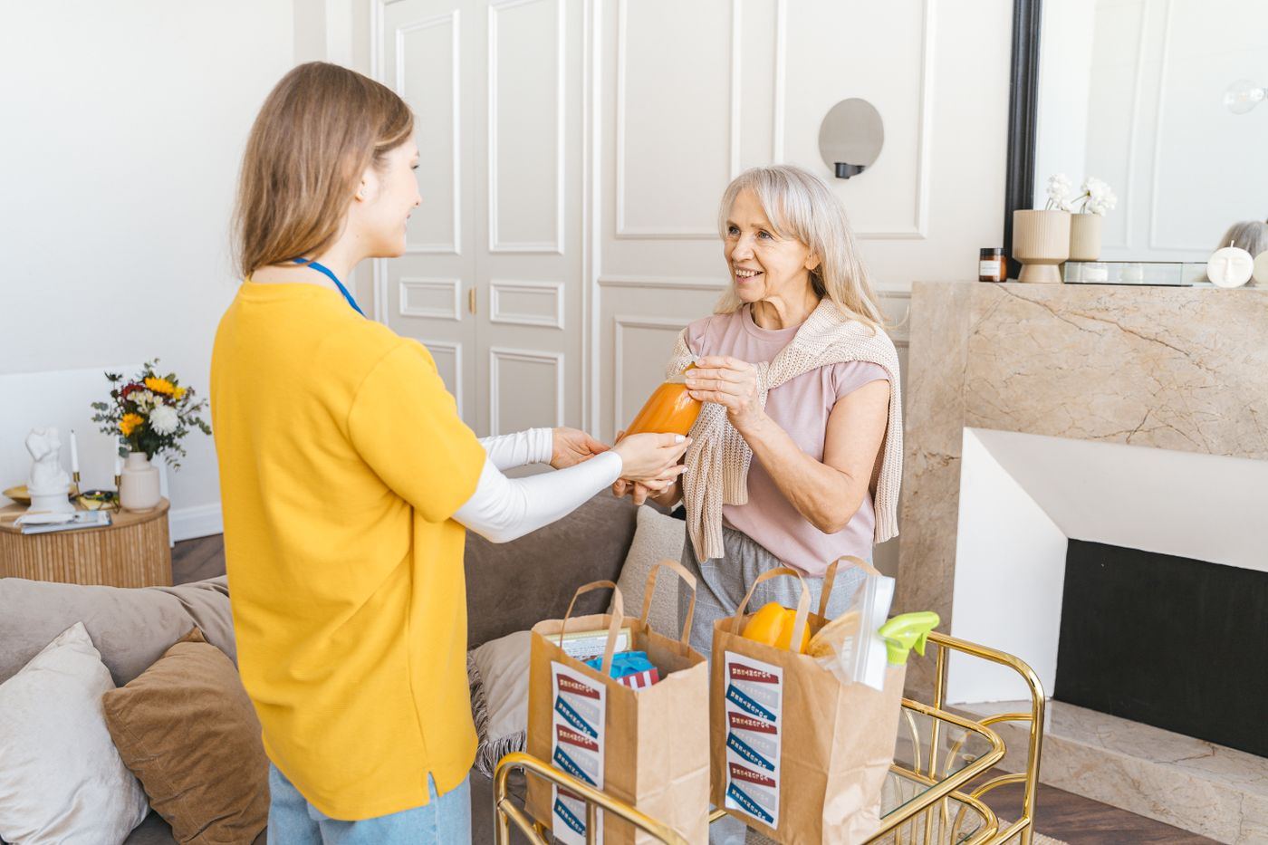 Caregiver sharing a laugh with a smiling senior woman while helping with groceries in her home