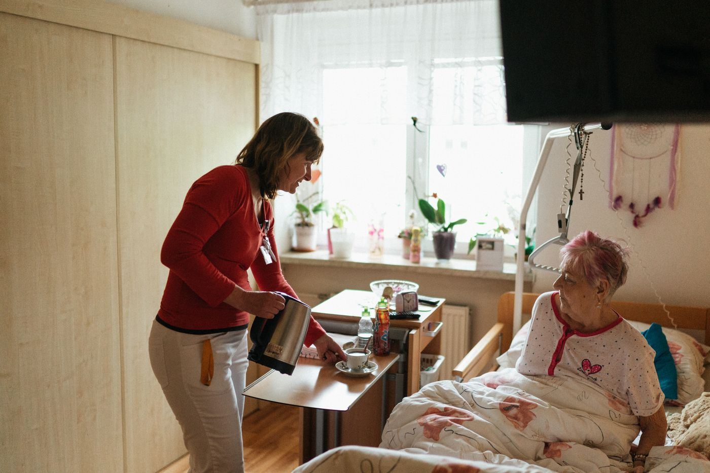Caregiver bringing tea to a senior woman in her sunlit bedroom at home